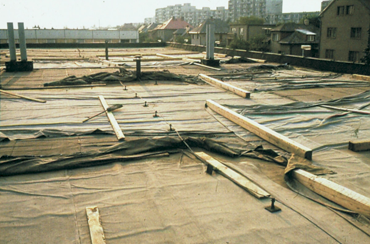 Obr. 3: Zoufalý pokus o zabránění průsaků do budovy školy v Čimicích. Plachty zatížené trámky na bezspádové (!) střeše s polystyrenovou termoizolací