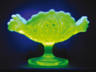 Obr. 5: Mísa na ovoce z uranového skla byla vyrobena v Austrálii v roce 1950. Sklo obsahuje stopy oxidu uraničitého, při nasvícení UV světlem mísa vyzařuje zelené fluorescenční světlo. Přítomnost uranu způsobuje také mírnou radioaktivitu objektu, v těchto koncentracích však lidské zdraví není nijak ohroženo.