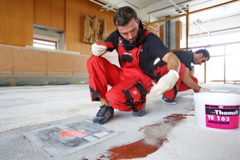 Pro lepší přilnavost následně nanášené vyrovnávací hmoty a vytvoření mimořádně pevného spojení podkladu se stěrkou posypal tým firmy Waschke ještě čerstvou pryskyřici vysušeným křemičitým pískem o zrnitosti 0,3–0,7 mm