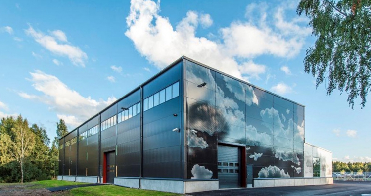 Celkový pohled na budovu HAMK, motiv mraků odkazuje na oblohu a dává budově nezaměnitelný vzhled, díky kterému i „obyčejná“ hala zapadá do okolního prostoru