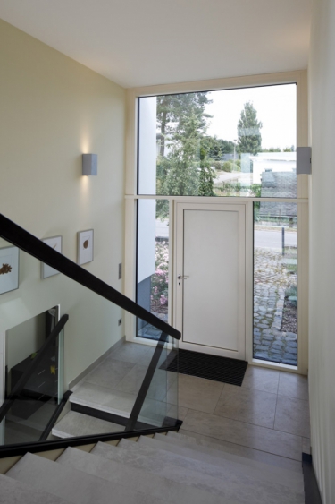 Hlavní vstup do členitého interiéru domu s vchodovými dveřmi, vybavenými biometrickou čtečkou otisků prstů Schüco Fingerprint