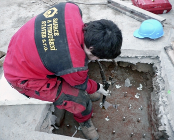 Realizace zpevnění podloží pod roznášecími bloky ŽB sloupů ve 2. NP, přenášejících zatížení do zesilovaných pilířů v 1. NP – původní stav s kamenným blokem základu a dřevěným sloupem s ocelolitinovou patkou (vlevo) a zpevňující injektáž centrální části zhlaví pilířů pryskyřicí CarboPur WF z úrovně 2. NP (vpravo)