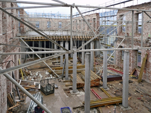 Pohled do vnitřního prostoru objektu v době budování vestavby 2. a 3. NP. Železobetonové sloupy středního traktu jsou založeny na roznášecích betonových blocích, jejichž podloží bylo před tím zpevněno injektáží pryskyřicí CarboPur WF. Ocelové ztužující prvky zajišťovaly stabilitu obvodových zdí po vybourání všech vnitřních konstrukcí.