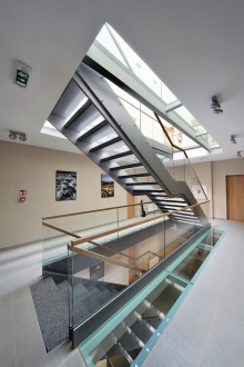 V místě křížení obou hmot objektu vzniklo komunikační jádro se schodišťovou halou a výtahem