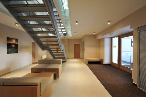 V místě křížení obou hmot objektu vzniklo komunikační jádro se schodišťovou halou a výtahem