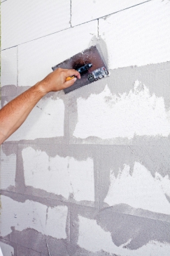 Zpracování omítky Ratio Slim: a) Rozmíchanou hmotou nejprve zapravíme větší spáry, ulomené rohy tvárnic a jiné nerovnosti