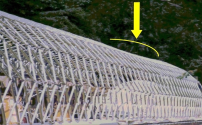 Obr. 9a: Příhradovina zdeformovaná od připevněného skleněného pláště. Styk, který měl působit dle návrhu jako samosvorný, ale jeho konstrukce takové působení ve všech směrech neumožňovala. Styk po přivaření všech ramen styčníku ke kuželovým koncům prutů byl schopen přenést působící zatížení prosklení.