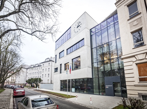 Přístavba je umístěna na hraně parcely školy, nové křídlo průčelím navazuje na historickou budovu, dále se pak zalamuje podél pozemku směrem do vnitrobloku