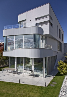 Kovový plášť vily člení skleněná zábradlí a dobře zvolený rytmus oken, která jsou téměř v líci obvodového pláště