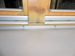 Obr. 5: Chybně osazený vnější hliníkový parapet – malý sklon parapetu (pod 6 °, viz voda stojící na parapetu); hniloba v konstrukčním spoji sloupku; parapet není tepelně separován od dolního vlysu okenního rámu. což vede k tvorbě rosného bodu a zvyšování vlhkosti a následně k separaci lazury a tvorbě plísní.