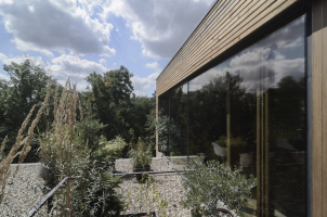 Horní kvádr má dřevěný obklad z horizontálně kotvených hoblovaných smrkových střešních latí, konstrukce zasklení jsou založeny na strukturálním fasádním systému s tmelenou spárou