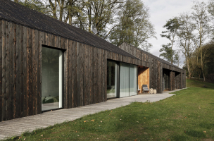 Dlouhou horizontální hmotu stavby spojuje tmavě opálené dřevo na fasádě i na střeše