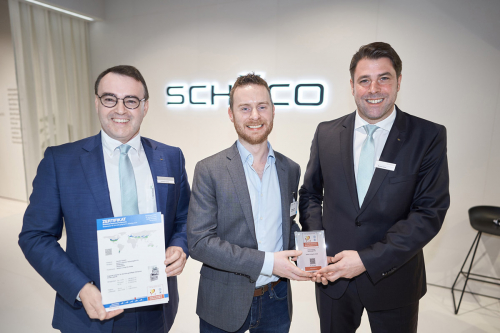 Edward Lowes (uprostřed) z Institutu pasivních domů (Passivhaus Institut) předává certifikát Markusi Herbstovi (vpravo), mluvčímu výkonného vedení společnosti Schüco Polymer Technologies KG, a Christianu Fischerovi (vlevo), vedoucímu technologického oddělení společnosti Schüco Polymer Technologies KG