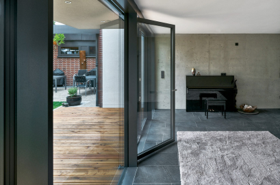 Fasáda tvořená prosklenými panely na výšku celé místnosti, které zahrnují i velkoformátové otvíravé části, umožňuje splynutí interiéru s venkovním prostorem (Schüco AWS 35 PD.SI)