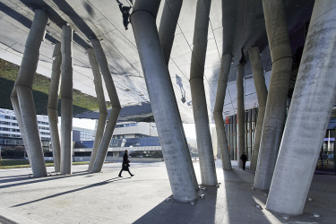 Exteriérový podhled tvoří zrcadlově lesklá kovová plocha, která v kombinaci s umělým osvětlením a vodním prvkem v dlažbě opticky zvyšuje šestimetrovou světlost u hlavního vchodu