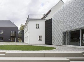 V zadní části pozemku stojí kolmo k ulici tmavý provozní dům, jeho střecha i plášť jsou z černých vláknocementových šablon