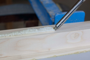 Nanášení lepidla na podklad. Při plošném lepení např. ve tvaru housenek.