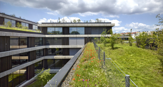 Lehké dřevěné lamely, subtilní rámy velkoformátových oken a dřevěné perforované akustické panely z vnitřní strany meziokenních vložek kontrastují s přirozeně stárnoucími betonovými římsami. Díky automatickému systému otvíravých částí fasády lze interiéry po většinu roku přirozeně větrat.