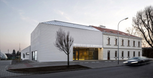 Předprostor budovy tvoří nástupní plocha dlážděná drobnou žulovou mozaikou různých odstínů, která zdůrazňuje význam budovy oproti okolní zástavbě. Fasádu nových částí domu tvoří omítka profilovaná do horizontálních říms o průřezu pravoúhlého trojúhelníku.