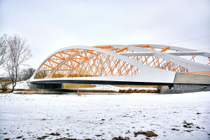 Tvarově i staticky vyvážená křivka oblouku elegantně přechází do protažených mostních křídel lehce zasazených do okolních břehů