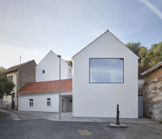 Místo má genius loci ulice v někdejší vesnici za Prahou. Původní domek zůstal zachován, architekti dále pracovali s podobnými hmotami. Rodinný dům tedy tvoří tři objekty, novostavby jsou umístěny směrem do svahu