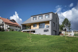 Ustupující 1. NP vytváří kryté loubí a terasu, na střeše obrácené k jihu je velký vikýř. Plášť domu je sjednocen se střešní krytinou šablonami z hliníkového plechu