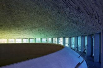 Kruhová asymetrická klenba s otiskem dřeva se neustále proměňuje v závislosti na úhlu a síle slunečních paprsků. Okna mají hliníkové, místy skryté rámy