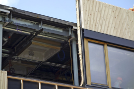 Na podélné plnostěnné vazníky se připevnily kotvy pro zavěšení lehkého dřevěného obvodového pláště o tloušťce 24 cm. Výroba prefabrikátů probíhala za pomoci CNC technologií, takže bylo dosaženo vysoké přesnosti a kvality. Hlavní předností systému ENVILOP je nicméně rychlost realizace – obvodové panely o rozměrech 3 x 3,6 m na stavbu přijížděly zkompletované s okny a fasádami. Při osazování byly panely zavěšeny na kotvy pomocí rektifikačních šroubů. Ocelové kotvy pro obklad se do zdiva připevnily přes podložku termostop.