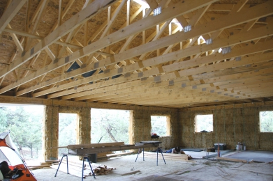 Obr. 3: Věnec stabilizující zdivo z nosné slámy. Dveřní rámy volně procházejí otvory ve spodním bednění věnce (OSB), aby nebránily kompresi balíků střechou.