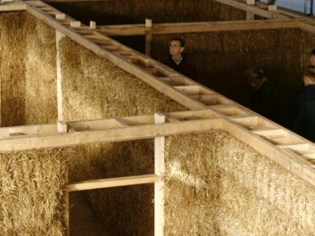 Obr. 4: Věnec stabilizující zdivo z nosné slámy. Dveřní rámy volně procházejí otvory ve spodním bednění věnce (OSB), aby nebránily kompresi balíků střechou.